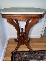 Full view of the side table showing white marble top and wooden base with carved details. Visible scratches on marble and wood with some missing parts on base.