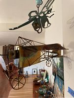 Hand holding metal vintage-style wireframe airplane sculpture showing the front and top sides with visible patina and intricate wire construction.