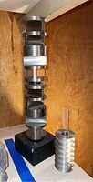 Tall metal sculpture with vertical stacked geometric shapes on a black base, polished silver finish