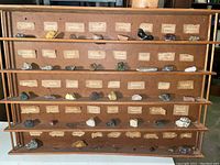 Wooden rack with many labeled mineral specimens lined up on shelves, showing the full collection layout.