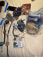 Full view of assorted jewelry items laid on fabric including necklaces, chains, a Lorus watch, pouches with beaded necklaces, and small boxes with rings.
