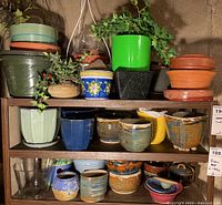 Full view of wooden shelves holding pottery and ceramic pots of various colors and sizes, some with faux plants.
