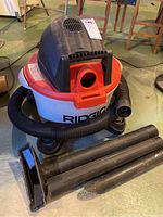 Wet/dry vacuum showing front, black hose, and multiple vacuum attachments laid in front.