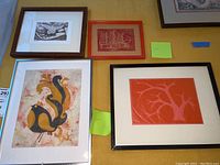 Four framed art prints arranged on a table showing different styles and colors of frames including wood, red, black, and white. Prints include stylized animals and abstract tree shapes.