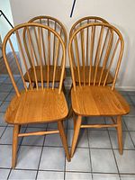 Four light wood chairs with curved spindle backs and flat seats placed on tiled floor.