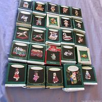 Photo showing arrangement of all 25 Hallmark miniature Christmas ornaments in original boxes spread on surface, green and black boxes with ornament images