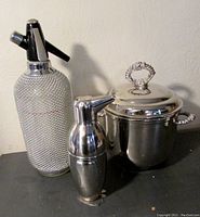 All three items arranged: seltzer bottle with chain mail covering, penguin-shaped cocktail shaker, sterling plated ice bucket.
