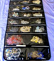 Full view of multi-pocket black zippered jewelry organizer holding multiple pieces of vintage costume jewelry, including brooches, necklaces, bracelets, and earrings.