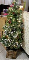 Full view of 4-foot pre-lit artificial Christmas tree with snow flocking, pine cones, red berries, and decorative box base, placed indoors.