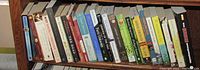 Wide angle photo showing 21 paperback books on a bookshelf, showcasing a variety of best-selling titles in good condition.