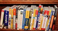 Photo showing the full row of 22 travel books with titles visible, arranged on a shelf.