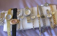 Top view of 11 women's dress watches arranged horizontally showing variety of styles including metal bracelets, mesh band, leather strap, and rhinestone decoration
