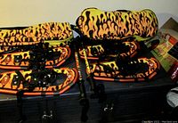 Photo displaying two pairs of kids/youth snowshoes with flame pattern, one set of adjustable poles also with flame design, and two protective backpacks featuring the same flame pattern.