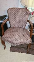 Front view of decorative antique accent arm chair showing fabric upholstery with nail head trim and carved wooden arms and legs. Upholstery shows signs of fraying and wear.