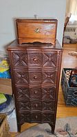 Front view of small wooden box with eagle emblem on top of ornate carved chest with 5 drawers