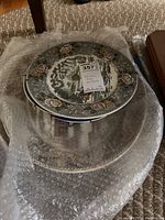Stacked decorative plates on bubble wrap showing the top plate with floral accent design and scenic center