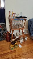 Maple wood end table with spindle sides and bottom shelf, top surface and lower shelf visible with various items around it.