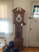 Full frontal view of the Ethan Allen grandfather clock standing near a door and curtain.