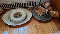 Five Goodwin Pottery plates with gold trim and woodland animal center designs displayed along with copper-tone baking molds, tin basket, and serving platters on a wooden floor.