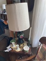 Full view of vintage floral table lamp on wooden side table with lace doily, showing surrounding candleholders and candles