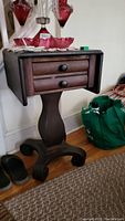 Front view of the vintage dark wood side table showing the two drawers with round knobs and the pedestal base with four legs.