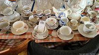 Photo showing an assortment of teacups, saucers, and teapots placed on a checkered tablecloth, including Japanese and Limoges china.