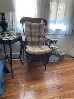 Full front view of the vintage wooden armchair with plaid cushioned seat and back, chamber pot visible underneath the seat.