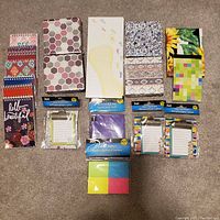 Assorted note pads and sticky notes featuring colorful and patterned covers laid out on floor.