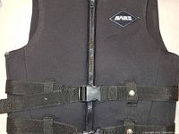 Front view of black life jacket vest showing zippered front and dual adjustable straps with plastic buckle for tightening fit.