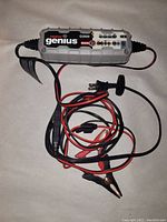 Full view of NOCO Genius G3500 smart battery charger with red and black clip cables and power plug laid out on white background.
