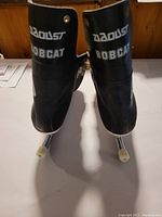 Front view of the black Daoust Bobcat ice skates showing the branding and metal blades with plastic guards.