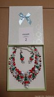 Set in open box showing necklace with Santa-claus, holly, and red berries design, and matching stud earrings.