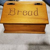 Closed solid wood bread box with 'Bread' carved on lid, showing front view