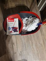 O-Cedar EasyWring microfiber spin mop fully assembled with bucket and box shown on hardwood floor.