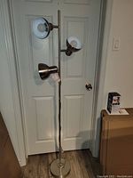 Full view of chrome tri light floor lamp with three cone-shaped adjustable heads and round base, placed in front of a white double door.