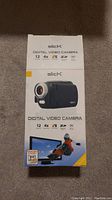 Original retail box of Slick digital video camera showing 12MP, 4X digital zoom, SD card compatible, and built-in LED light features.