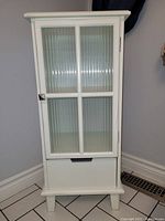 Front view of the closed white bathroom cabinet showing frosted ribbed glass door with six pane design and a drawer at the bottom.