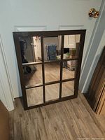 Full view of the brown wooden vintage mirror showing all 9 glass panes and the frame, placed on a hardwood floor leaning against a white door.