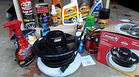 Coleman orbital waxer and assorted car cleaning products including sprays and bottles, organized on concrete ground.