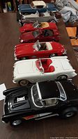 Seven die cast model cars arranged in a line showing variety of colors and designs including Corvettes and vintage styled cars.