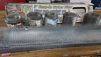 Metal mesh gutter guard rolls and three rolled 3-foot snap-in gutter filters with their box in the background