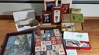 View showing multiple Hallmark Keepsake ornaments, Matchbox Melodies musical ornaments in boxes, a wooden block calendar, and framed artwork arranged together on a table.