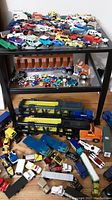 Wide view of table and floor filled with various scale die-cast cars and haulers spread out showing quantity and variety