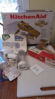 Vintage KitchenAid slicer in box with accessories displayed including a rolling pin, idea book, electric tool, red food holder, and cutting board.