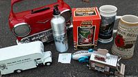 Photo showing the assortment of beer mugs, toy trucks, bottle with pump, and miniature trailer model arranged on pavement