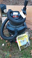 Full view of black Shop Vac vacuum with hose attached. Replacement vacuum bags in original packaging visible in front of vacuum.