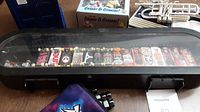 Wide shot of collection showing fingerboards inside the black display case with transparent lid, arranged in a row with various colorful deck designs.