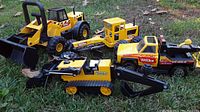 Overview of all four Tonka trucks arranged on grass showing different angles and scale, including bulldozer, excavator, backhoe loader, and dump truck.