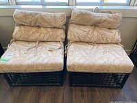 Front view of two bamboo chairs side by side, showing cushioned seats and backs with leaf-patterned beige fabric.