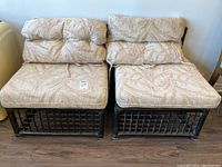 Front view of two black bamboo lounge chairs placed side by side, each with cream-colored cushions featuring a leaf pattern tied onto the frame.